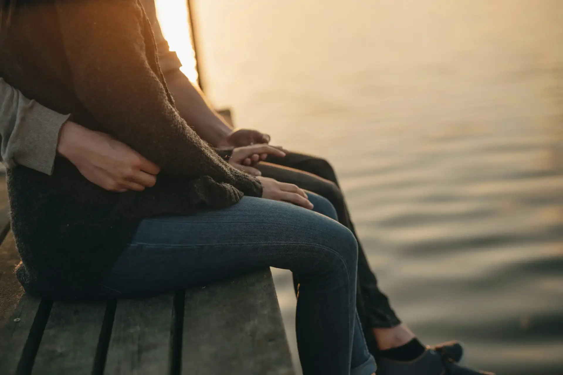 Paar sitzt eng umschlungen am Wasser im Sonnenuntergang – Nähe trotz einseitigem Kinderwunsch