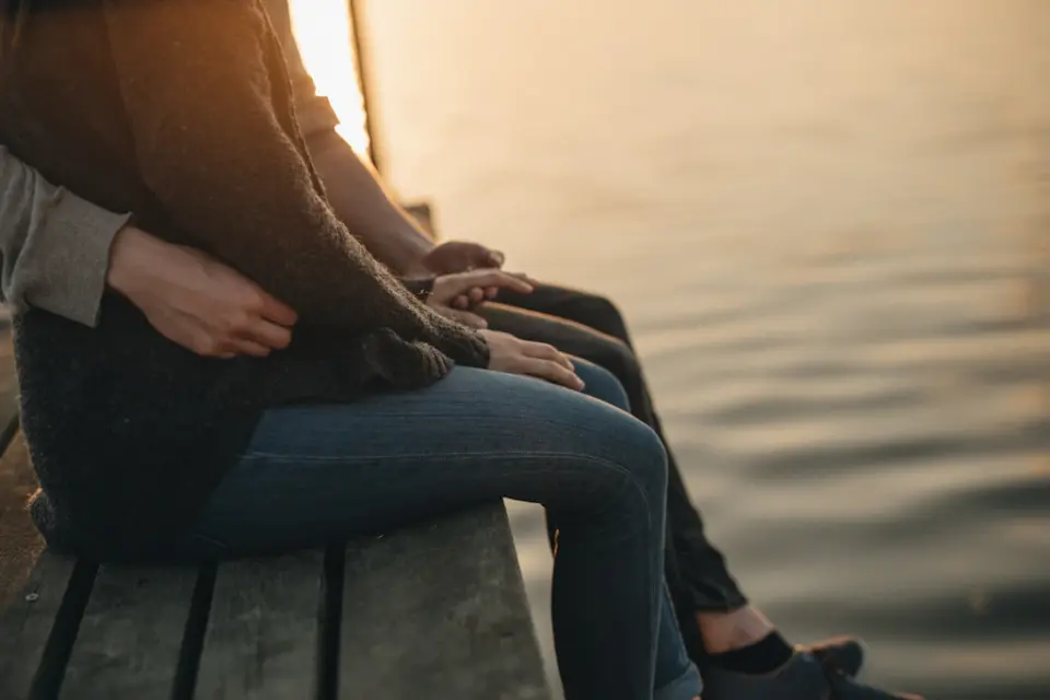 Paar sitzt eng umschlungen am Wasser im Sonnenuntergang – Nähe trotz einseitigem Kinderwunsch