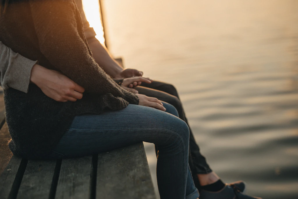 Paar sitzt eng umschlungen am Wasser im Sonnenuntergang – Nähe trotz einseitigem Kinderwunsch
