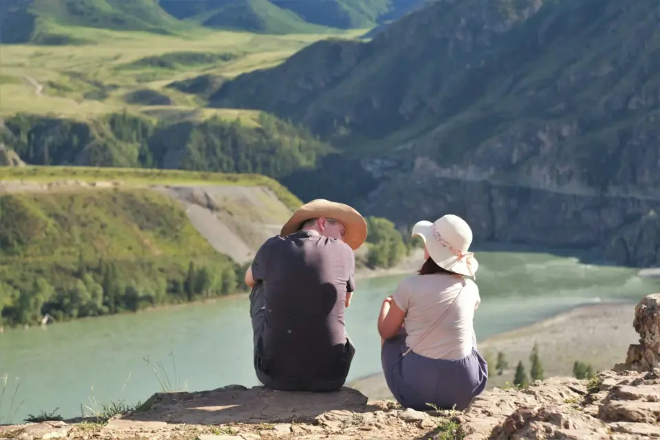 Paar sitzt gemeinsam auf einem Felsen über einem Fluss und blickt in die Landschaft: kinderlos glücklich als bewusste Entscheidung