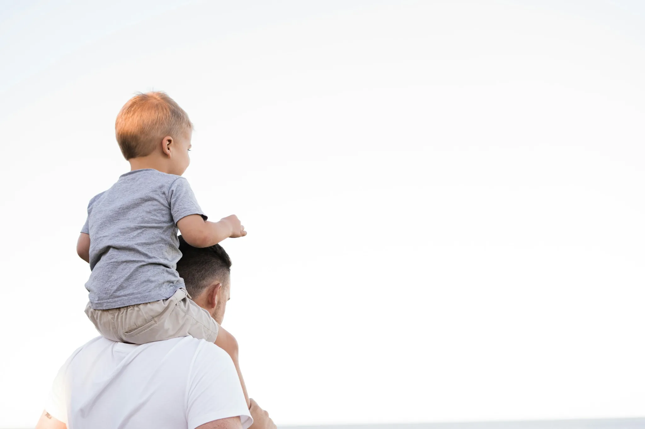 Kind sitzt auf den Schultern seines Vaters vor hellem Himmel: Klarheit in der Frage nach einem zweiten Kind