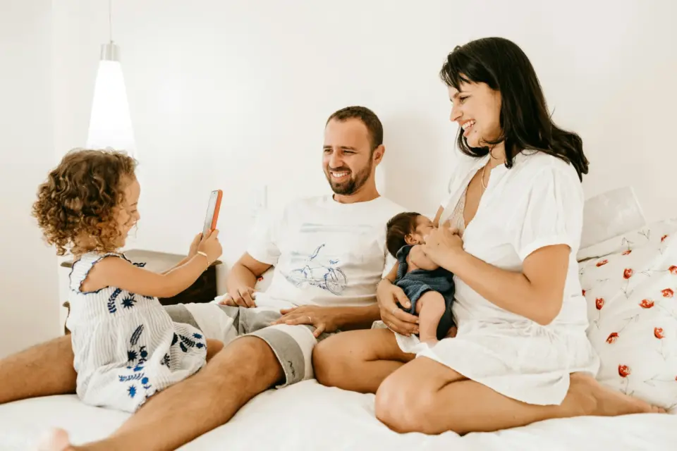 Eltern mit Kleinkind und Baby sitzen entspannt zusammen auf dem Bett: Familienalltag mit zwei Kindern